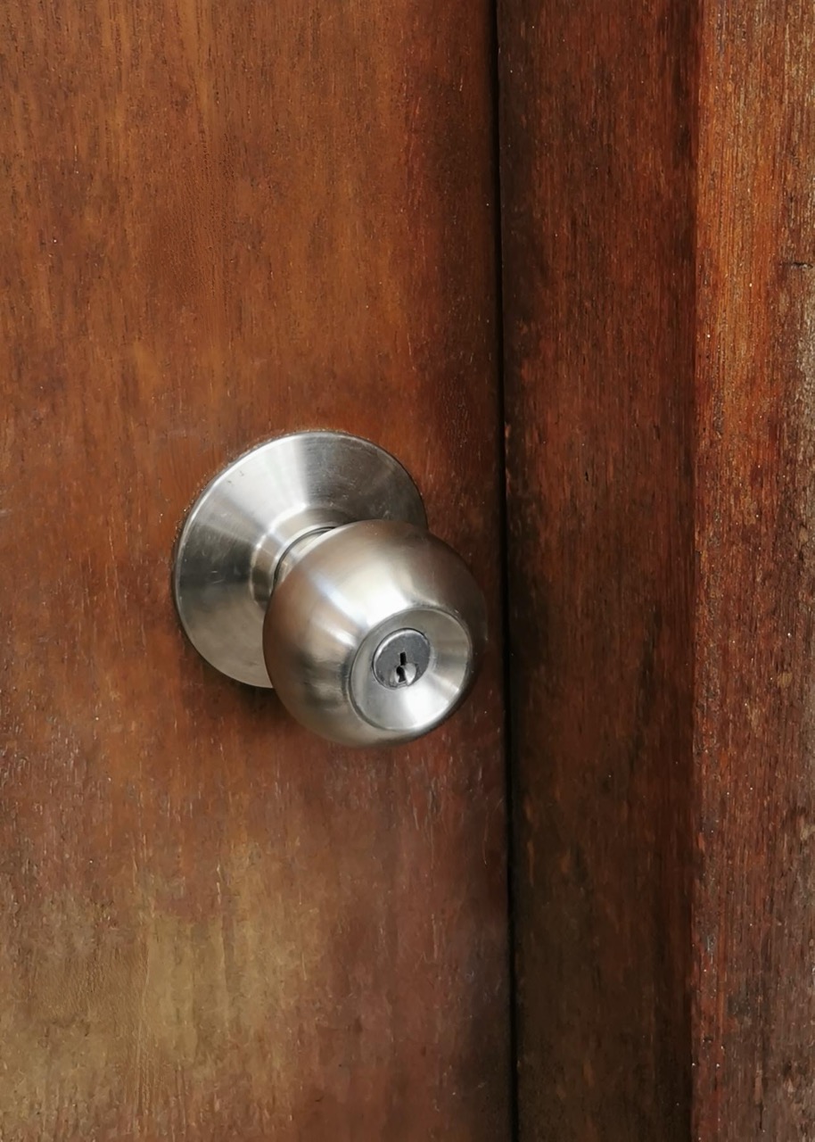 Stainless cylindrical door knob fitted to a wooden door.