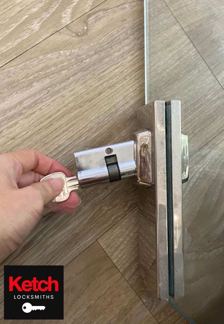 Hand inserting key into a glass-door cylinder lock during fitting.