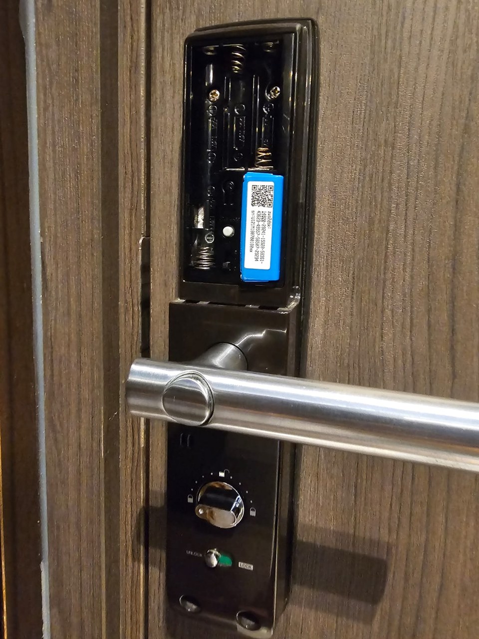 Digital lock with the battery compartment open beside a stainless lever handle.