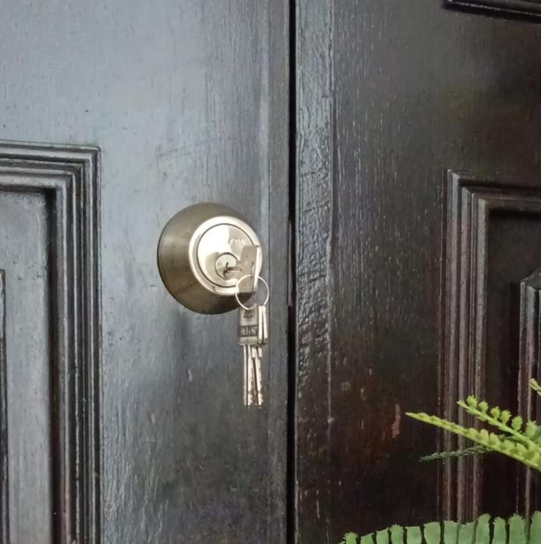 Single-cylinder deadbolt fitted to a black main door, with keys in the lock.